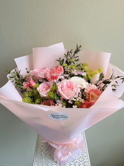 A delicate bouquet with pink roses, carnations, lisianthuses, and greenery in soft pink wrapping.