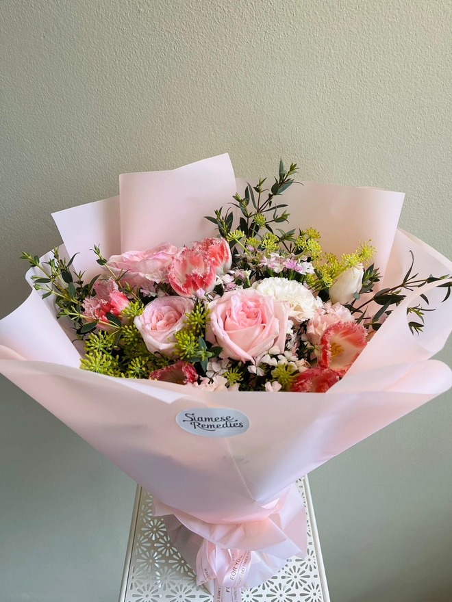 A delicate bouquet with pink roses, carnations, lisianthuses, and greenery in soft pink wrapping.