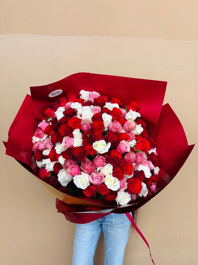 A large bouquet of red, pink, and white roses wrapped in bold red paper.