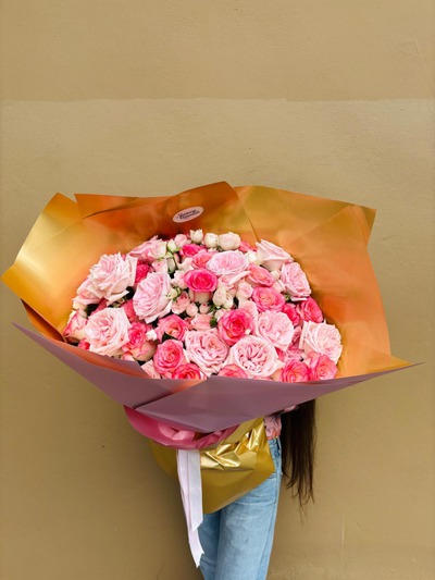 A bouquet of lush pink roses wrapped in golden and pink paper.