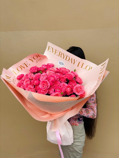 A grand bouquet of vibrant pink roses wrapped in elegant peach paper with gold lettering.
