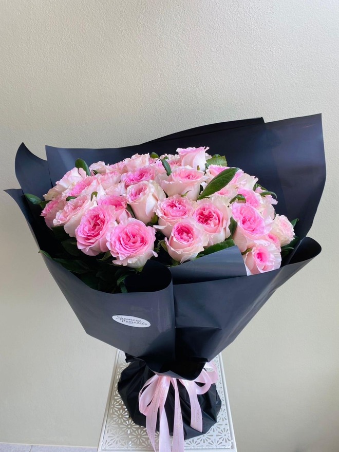 A bouquet of soft pink roses wrapped in black paper with a pink ribbon. colors: pink,