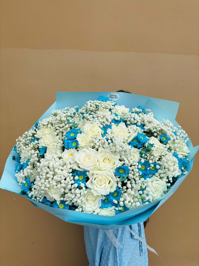 Bouquet of white roses, baby’s breath, and blue daisies wrapped in blue paper.