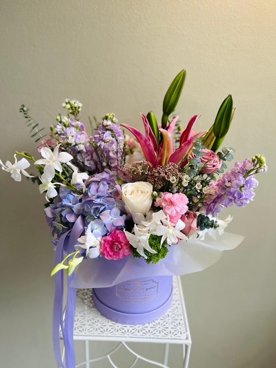 A pastel floral box featuring lilies, roses, orchids, carnations, and hydrangeas in pink, purple, and white.