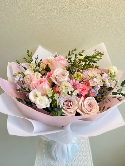 A delicate bouquet of blush and cream roses, lisianthuses, and carnations wrapped in pink and white.